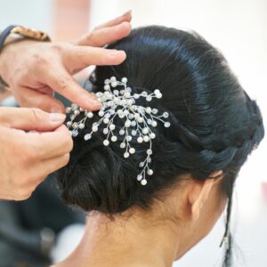 Photograph of a hairstylist arranging an elegant updo embellished with delicate decorative pins in a professional studio.